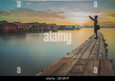 L'uomo turistico che prende selfie con il telefono delle cellule al villaggio di pescatori di Chew Jetty. Foto Stock