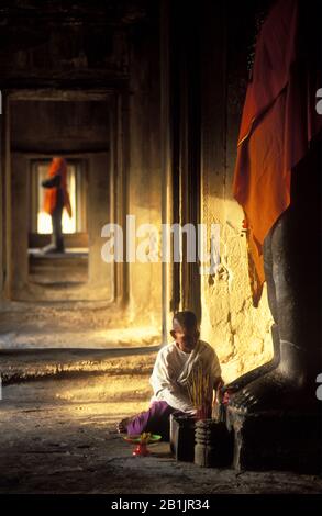 Angkor Wat Interno. Donna che mette offerte agli dei. Grandi statue di Vishnu vestite di tessuto arancione. Dawn, Foto Stock