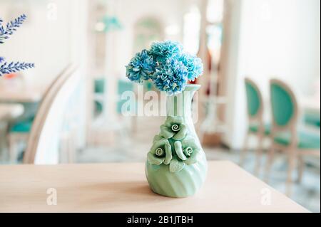 Un piccolo vaso di color menta con fiori di mais blu su un tavolo di legno in una luminosa e spaziosa camera con sedie blu Foto Stock