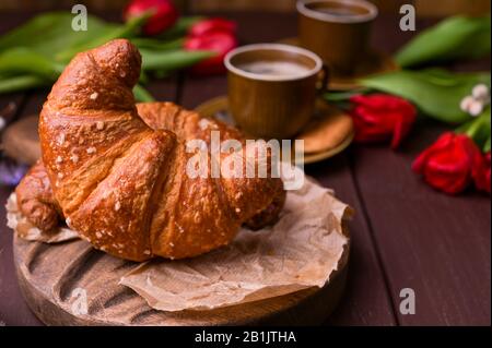 Colazione di Pasqua con caffè espresso fresco aromatico, croissant, uova colorate, tulipani rossi e salice. Caffè con dolci, fiori su un tavolo di legno. Spazio di copia. Foto Stock