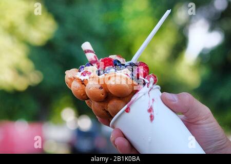 Bacca dado bolla waffle in tazza di carta bianca in mano su sfondo sfocato. Foto Stock