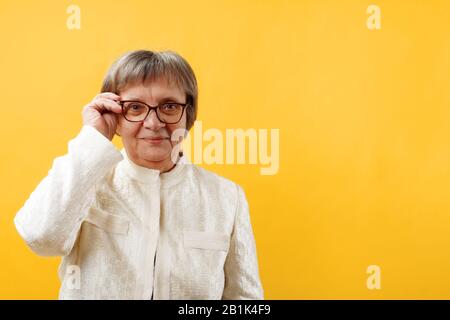 Donna matura senior in occhiali su sfondo giallo. Spazio di copia ravvicinato. Foto Stock
