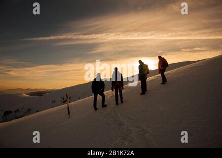 Silhouette escursionistica all'alba sul Monte Ciucas in inverno guardando il tramonto, parte della catena dei Carpazi rumeni Foto Stock