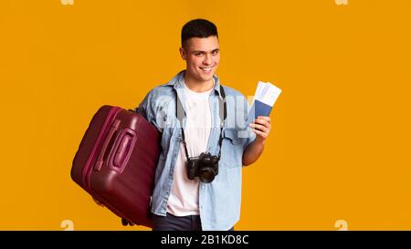 Turista sorridente con macchina fotografica e valigia con biglietto e passaporto Foto Stock