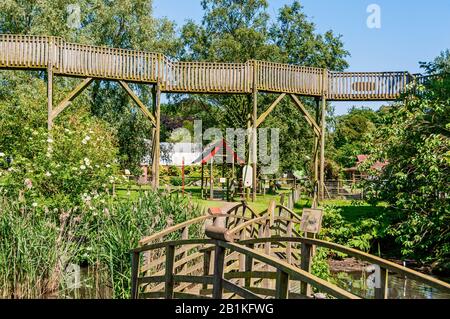 La passeggiata in legno di tigre si affaccia sui ponti ad arco e sulla vegetazione che attraversa una piscina mentre passa davanti a alberi verdi ancora più alti Foto Stock