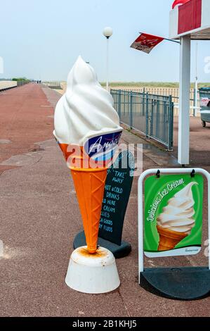 Un grande modello di pubblicità bianco e marrone di plastica di un cornetto gelato si trova fuori sale da tè come escursionisti lontani sono oscurati da nebbia di mare Foto Stock
