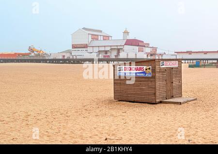 Un capannone in legno con due note dipinte di colori vivaci che fanno pubblicità a sedie a sdraio, ecc. si trova di fronte al molo Britannia avvolto dalla nebbia Foto Stock