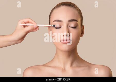 Mano Che Applica Le Ombre Oculari Alla Ragazza Usando La Spazzola Cosmetica, Studio Shot Foto Stock