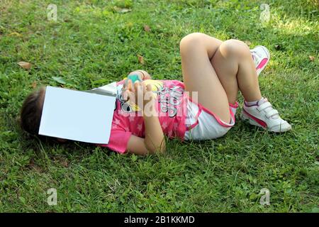 bambina sdraiata con libro sul suo viso Foto Stock