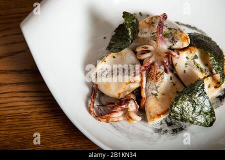 Calamari grigliati con salsiccia nera saltata, cipolla candita e alghe croccanti nori servite in porcellana bianca. Nuova cucina, immagine isolata Foto Stock