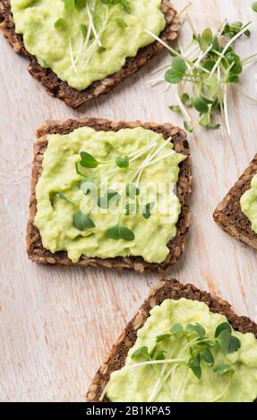 Spuntini vegetariani con avocado e microcreame su tavola di legno bianca rustica vicino Foto Stock