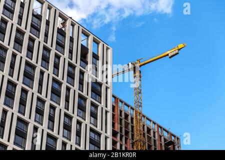 Costruzione di un moderno complesso residenziale. La costruzione di un edificio a più piani. Cargo gru su uno sfondo di cielo blu. Foto Stock