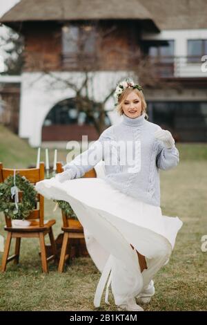 La sposa si trova vicino al tavolo da banchetto sullo sfondo del prato e della casa. Foto Stock