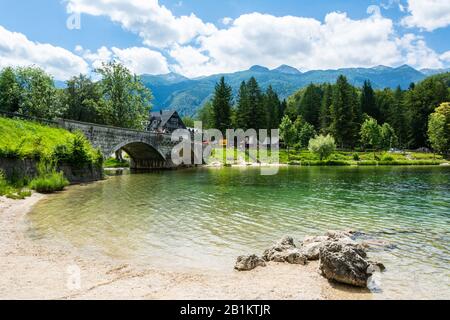 Ribcev Laz, Slovenia – 7 Luglio 2016. Vista sul lago di Bohinj in Slovenia, in estate. Vista con il ponte che attraversa il fiume Sava Bohinjka, persone e costruire Foto Stock