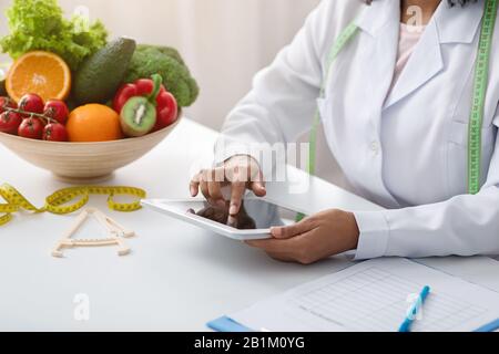 Dietologist donna nera che usa il tablet digitale sul posto di lavoro Foto Stock