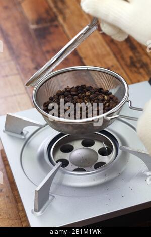 tostatura dei chicchi di caffè processo con un pratico tostatore a casa; controllo delle condizioni di tostatura dei chicchi di caffè Foto Stock