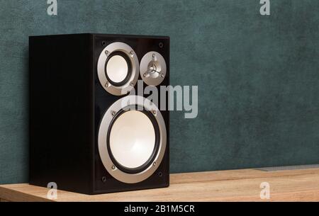 Un moderno altoparlante audio Hi-Fi nero a due vie all'interno su una scrivania in legno vicino alla parete verde scuro Foto Stock