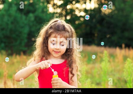 Cute Little Girl soffiare bolle di sapone in campo al giorno d'estate - concetto di infanzia felice Foto Stock