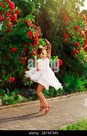 Bella bambina sta danzando fuori nel giardino estivo con rose. Foto Stock