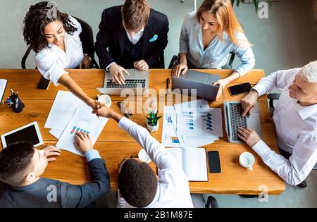 Businesswoman Scuotere Le Mani Con Il Collega Durante La Riunione In Ufficio, Top-View Foto Stock