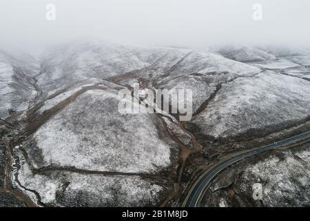 Strada di campagna tortuosa attraverso una valle circondata da montagne innevate Foto Stock