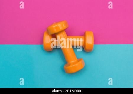 Due manubri arancioni su sfondo rosa e blu. Uno strumento per la formazione, lo sport e l'attività in estate. Foto Stock