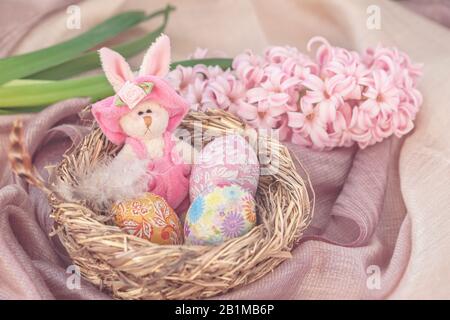 Bunnie di Pasqua in un nido d'uccello naturale con uova di Pasqua al cioccolato accanto a e fiore di primavera. Composizione per le vacanze di Pasqua Foto Stock