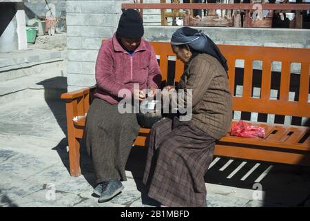 Donne Seduti su una panchina e Facendo Chores di famiglia su un caldo sole in Nepal Himalaya Mountain Village Foto Stock