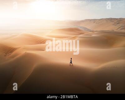 Donna che cammina sulle dune di sabbia del deserto vista aerea al tramonto Foto Stock