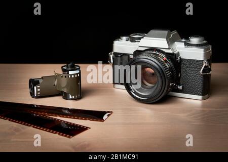 Vista frontale di una classica telecamera analogica da 35 mm con rotoli di film vintage e analogici su tavolo in legno Foto Stock