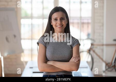 Lavoratore femminile con le braccia incrociate guardando la posa della macchina fotografica all'interno Foto Stock