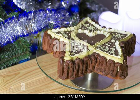 Torta a forma di stella appena sfornata con un cuore interno, decorata con cioccolato naturale e scaglie di mandorle, su un vassoio di vetro, su un tavolo di legno. Natale Foto Stock