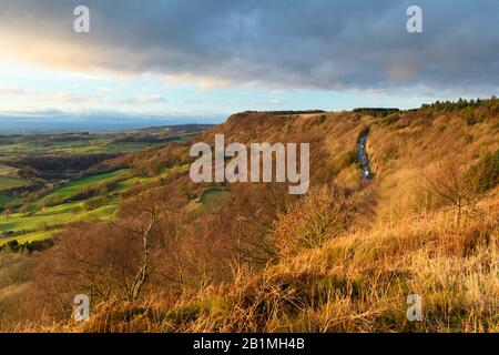 Splendida vista panoramica a lunga distanza della scarpata Sutton Bank illuminata dal sole, strada ripida, terreno agricolo e cielo drammatico - Roulston Scar, North Yorkshire, Inghilterra UK Foto Stock