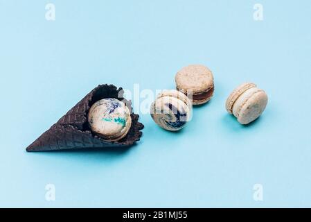 Macaroon assortiti in nero corno gelato su sfondo blu pastello con spazio copia. Immagine creativa e moody. Vista dall'alto, piatto. Foto Stock