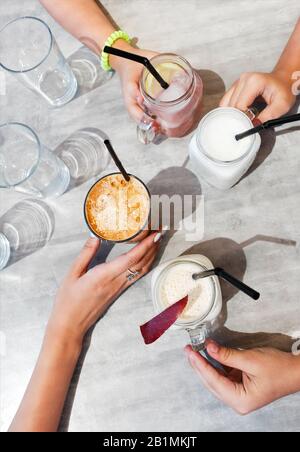 Vista dall'alto dei genitori anonimi e dei bambini che tengono tazze di bevande fresche fredde sul tavolo il giorno d'estate nel caffè Foto Stock