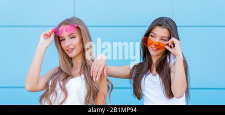 Due giovani hipster donna amici in neon retrò occhiali da sole in piedi e sorridente sulla parete blu Foto Stock