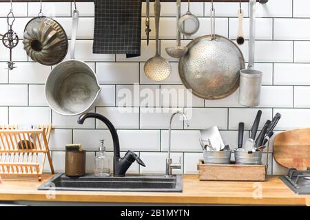 Vari utensili d'epoca disposti a parete e banconi vicino al lavello in accogliente cucina a casa Foto Stock