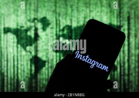 Il logo Instagram visualizzato sullo schermo dello smartphone con la mappa mondiale Matrix-like visibile sfocata sullo sfondo Foto Stock