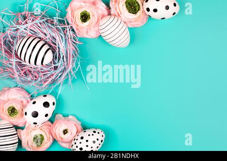 Nido decorativo con uova grafiche creative e fiori ranunculus su sfondo pastello blu. Concetto di Pasqua. Inserire il testo. Foto Stock