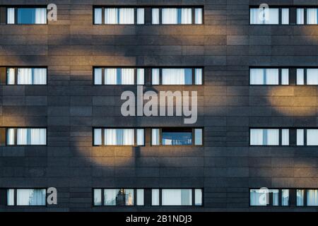 Luce del pomeriggio sulla facciata nera di un edificio urbano con lunghe finestre orizzontali Foto Stock