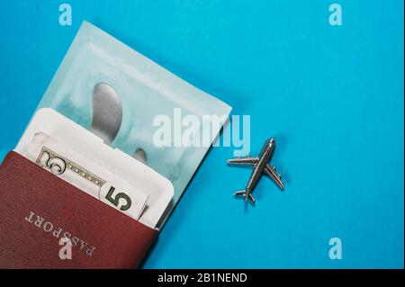 Oggetti obbligatori per viaggiare in aereo. Passaporto, contanti 5 fattura, macchie degli occhi e una figura metallica di un aereo su uno sfondo blu chiaro. Flatl Foto Stock
