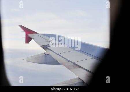 ala in aereo attraverso la finestra oblò su uno sfondo di cielo blu e nuvole bianche, mood toning Foto Stock