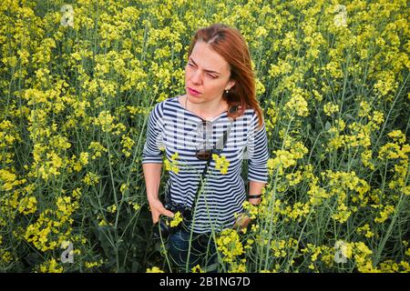 Fotografo femminile che indossa una camicia con strisce intorno al centro di un campo di colza. Foto Stock