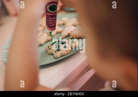 un bambino decora un biscotto preparato nella cucina con vernice verde commestibile da un tubo Foto Stock