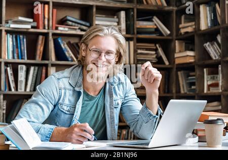 Ritratto giovane studente a casa biblioteca scrivania prendere appunti da manuale portatile. Foto Stock