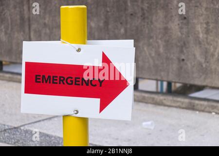 Vista ravvicinata del cartello di emergenza dell'ospedale in rosso con le frecce direzionali rivolte verso l'ingresso della sala di emergenza Foto Stock