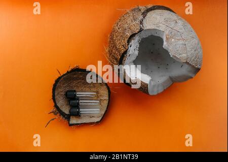 Cocco rotto maturo con polpa succosa su uno sfondo chiaro arancione chiaro, tre piccoli vasi per cosmetici o medicina in una conchiglia di cocco Foto Stock