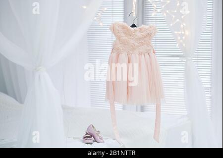 preparazione per la vacanza per la ragazza, un delicato abito in tulle rosa pesa su un appendiabiti su un leggero sfondo di letti e tende, rosa poco Foto Stock