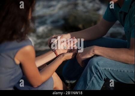 Un paio di mani di persone in amore tenere le mani e spostare pietre e conchiglie l'una verso l'altra estate contro il mare, una carta per San Valentino circa l'amore a Foto Stock