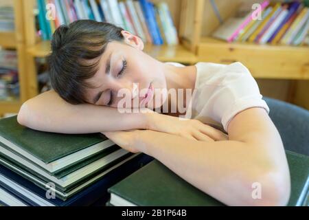 giovane signora addormentato su mucchio di libri in biblioteca Foto Stock